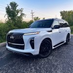 2026 Infiniti QX80 in Radiant White, front 3/4 view, lights on,