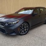2025 BMW M5 Touring in Frozen Deep Grey, front 3/4 view, lights on
